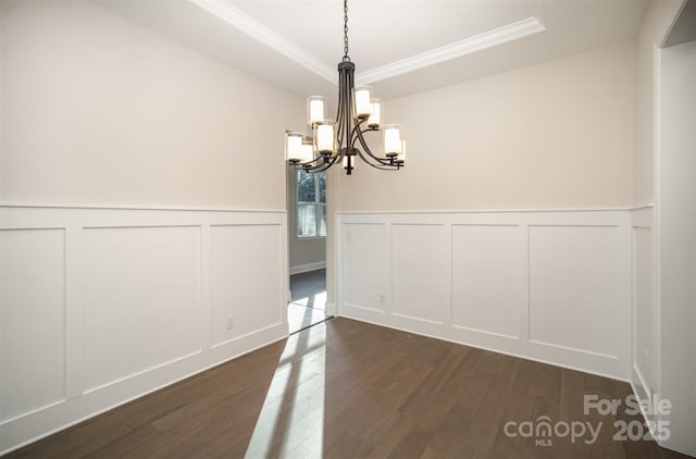 unfurnished dining area featuring a decorative wall, crown molding, a notable chandelier, and dark wood finished floors