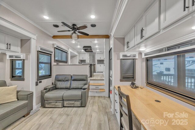 living area with light wood-type flooring, a ceiling fan, ornamental molding, and baseboards