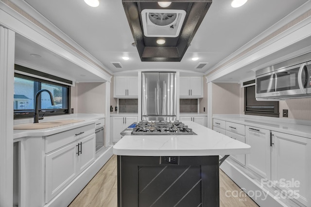 kitchen with stainless steel appliances, a sink, a center island, white cabinetry, and light wood-style flooring