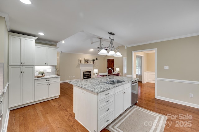 kitchen with stainless steel dishwasher, light wood-style flooring, a sink, a fireplace, and ornamental molding
