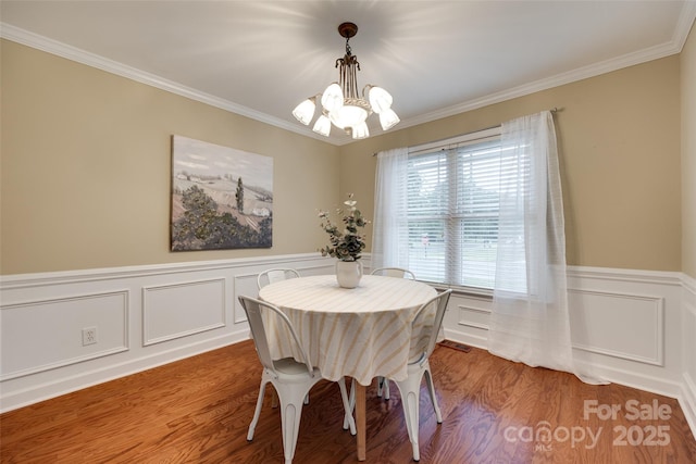 dining area featuring a chandelier, wood finished floors, crown molding, and wainscoting