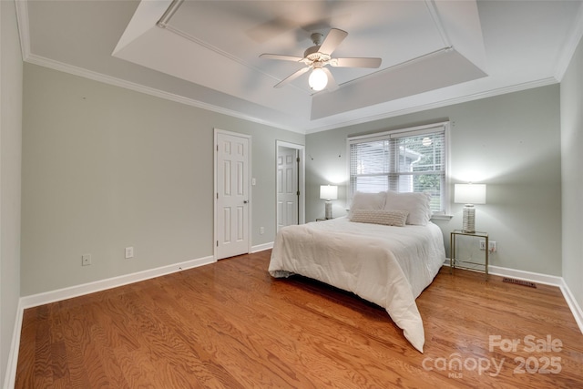 bedroom with a raised ceiling, wood finished floors, visible vents, ornamental molding, and baseboards