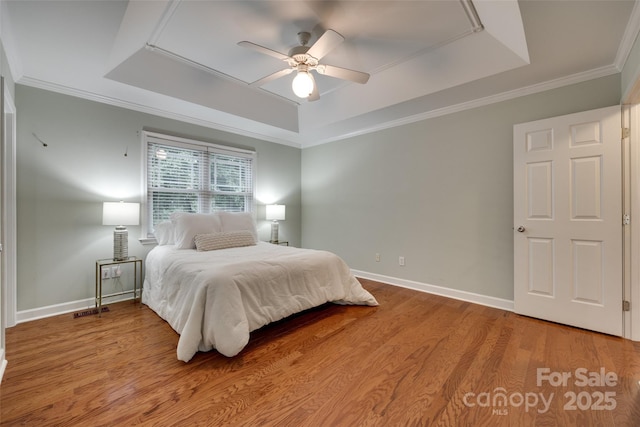 bedroom featuring a raised ceiling, wood finished floors, baseboards, and ornamental molding
