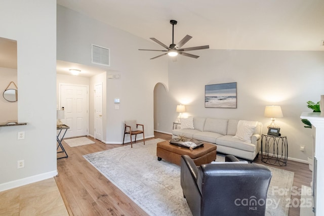 living area with light wood-style flooring, arched walkways, baseboards, visible vents, and ceiling fan