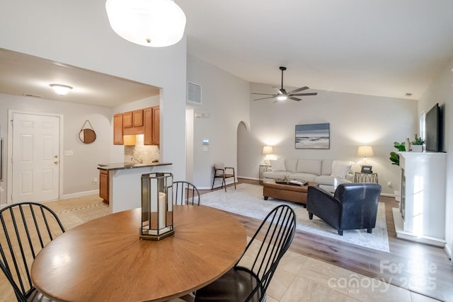 dining space featuring visible vents, arched walkways, baseboards, high vaulted ceiling, and ceiling fan