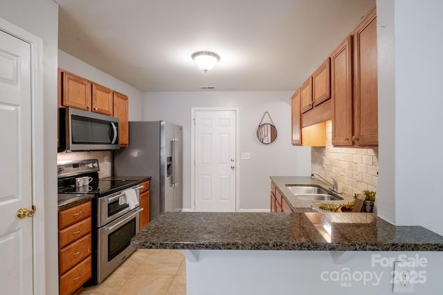 kitchen with a peninsula, a sink, appliances with stainless steel finishes, and tasteful backsplash