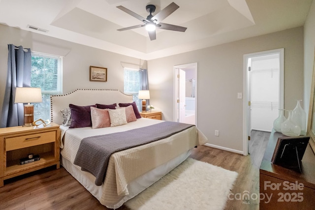 bedroom featuring ensuite bathroom, wood finished floors, a walk in closet, a raised ceiling, and visible vents
