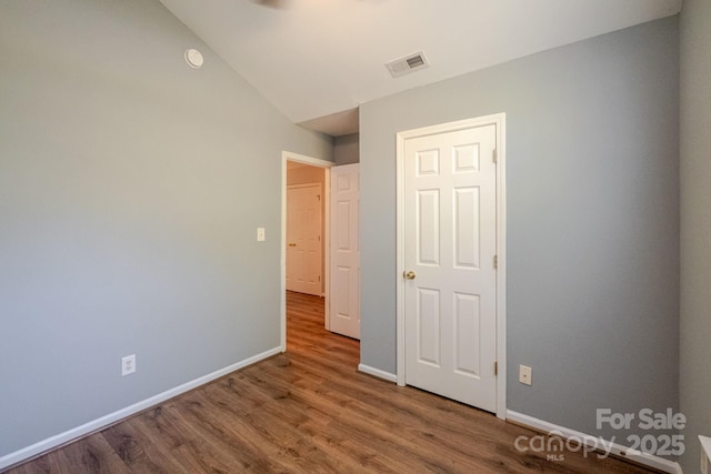 unfurnished bedroom featuring baseboards, wood finished floors, visible vents, and vaulted ceiling