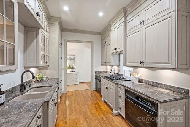 kitchen with a sink, light wood-style floors, black oven, dark stone counters, and glass insert cabinets