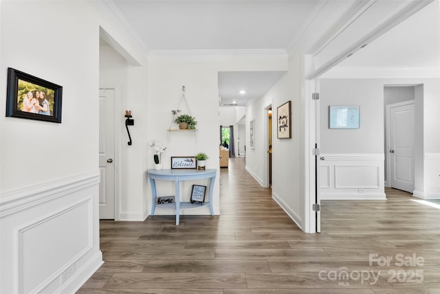 corridor with crown molding, wood finished floors, and a wainscoted wall