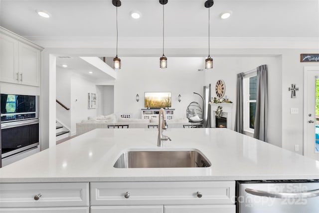 kitchen with a sink, stainless steel appliances, open floor plan, ornamental molding, and hanging light fixtures