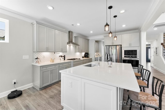 kitchen featuring a sink, stainless steel appliances, wall chimney range hood, ornamental molding, and gray cabinets