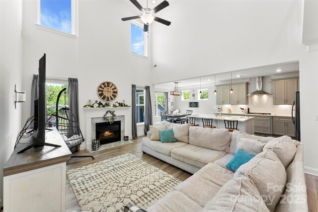 living area with a towering ceiling, ceiling fan, light wood finished floors, a high end fireplace, and recessed lighting