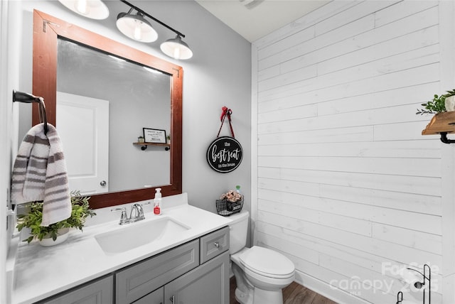bathroom featuring wooden walls, vanity, toilet, and wood finished floors