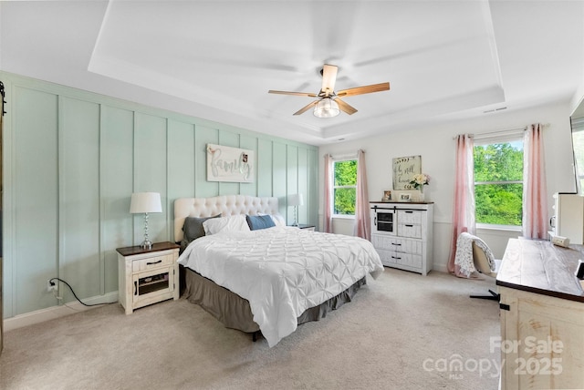 bedroom with a raised ceiling, light carpet, ceiling fan, and baseboards