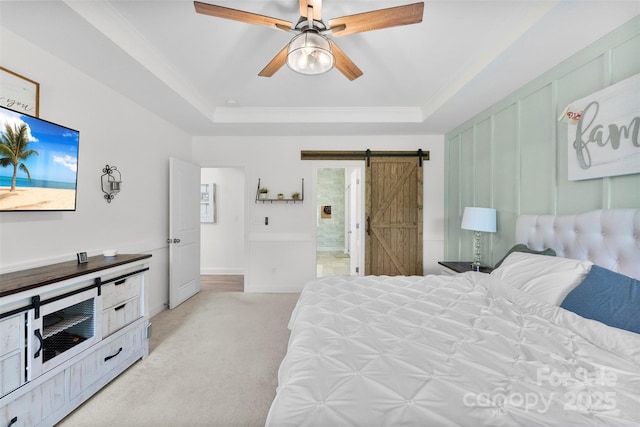 bedroom with a barn door, a raised ceiling, light carpet, ensuite bath, and ornamental molding