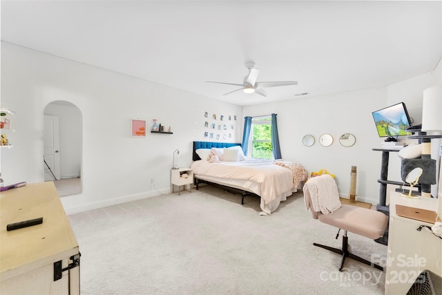 bedroom featuring arched walkways, light carpet, a ceiling fan, and baseboards