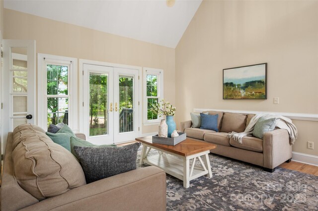 living area with baseboards, high vaulted ceiling, wood finished floors, and french doors
