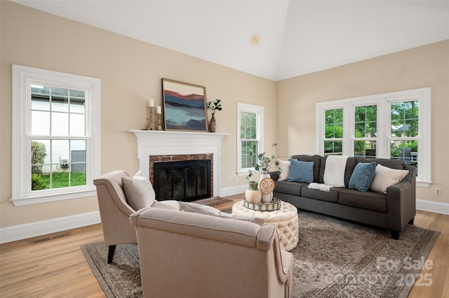 living room featuring light wood-style flooring, a brick fireplace, baseboards, visible vents, and high vaulted ceiling