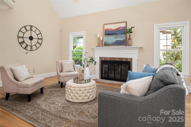 living room featuring baseboards, wood finished floors, lofted ceiling, and a brick fireplace