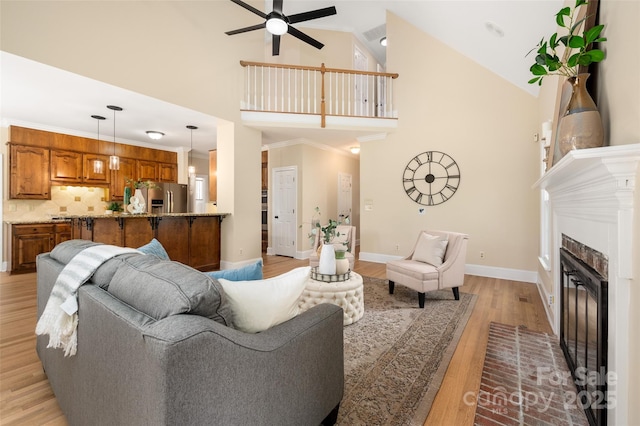 living area with baseboards, high vaulted ceiling, ceiling fan, and light wood finished floors