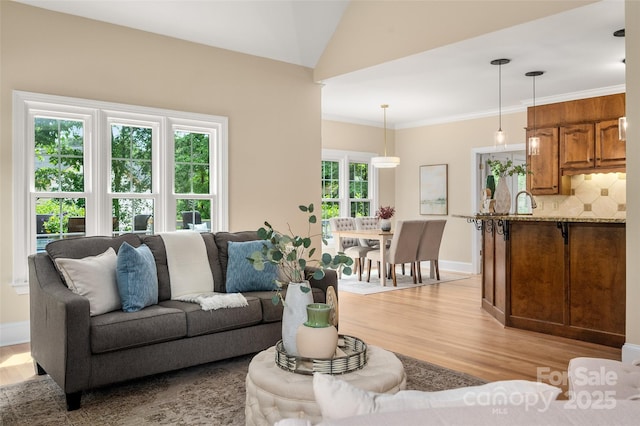 living area with baseboards, crown molding, lofted ceiling, and light wood-style flooring