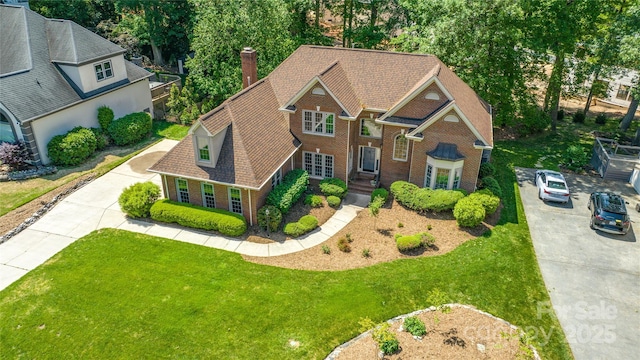 view of front of property featuring a chimney, brick siding, a front lawn, and concrete driveway