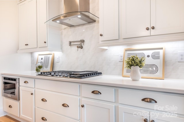 kitchen featuring light countertops, white cabinetry, wall chimney range hood, and stainless steel gas stovetop