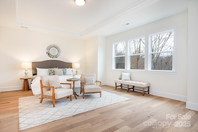 bedroom featuring baseboards, wood finished floors, a tray ceiling, and visible vents