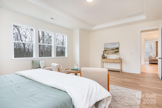 bedroom featuring light wood-type flooring, a tray ceiling, multiple windows, and visible vents