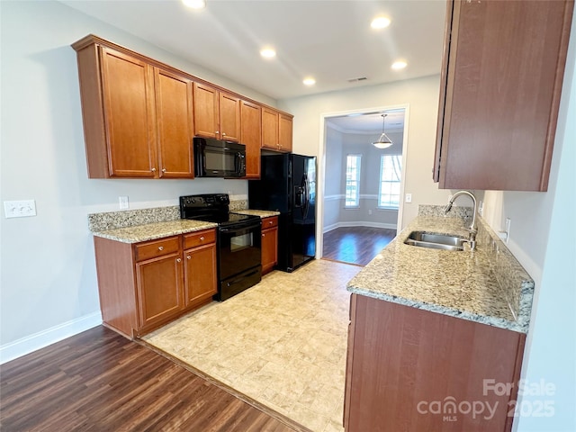 kitchen with brown cabinetry, baseboards, a sink, and black appliances
