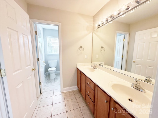 bathroom featuring toilet, a sink, double vanity, and baseboards
