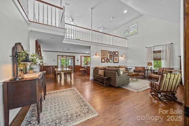 living room with wood finished floors, visible vents, a ceiling fan, wainscoting, and high vaulted ceiling