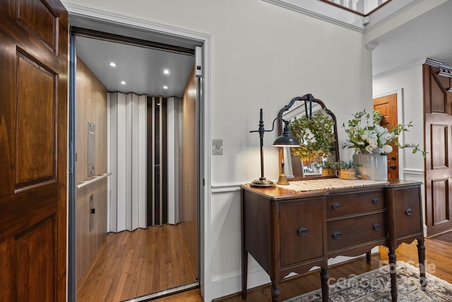 hallway featuring baseboards, elevator, recessed lighting, wood finished floors, and ornamental molding