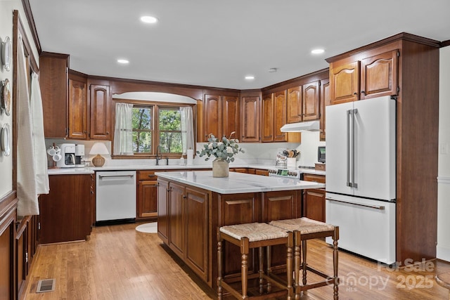 kitchen featuring a sink, light wood-style floors, dishwasher, under cabinet range hood, and freestanding refrigerator