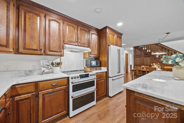 kitchen featuring light wood-type flooring, recessed lighting, high end appliances, brown cabinets, and under cabinet range hood