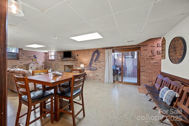 dining space featuring a drop ceiling and brick wall