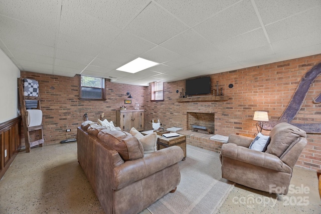 living area with a fireplace, a paneled ceiling, and brick wall