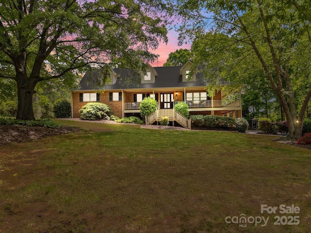 view of front of property featuring stairway, a lawn, brick siding, and a deck