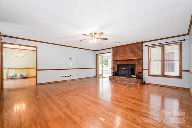 unfurnished living room featuring a brick fireplace, light wood-style flooring, ceiling fan with notable chandelier, baseboards, and ornamental molding