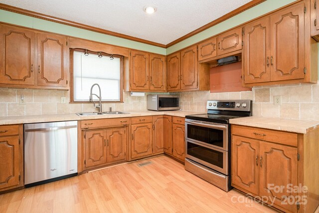kitchen featuring crown molding, brown cabinets, a sink, light wood-style floors, and stainless steel appliances
