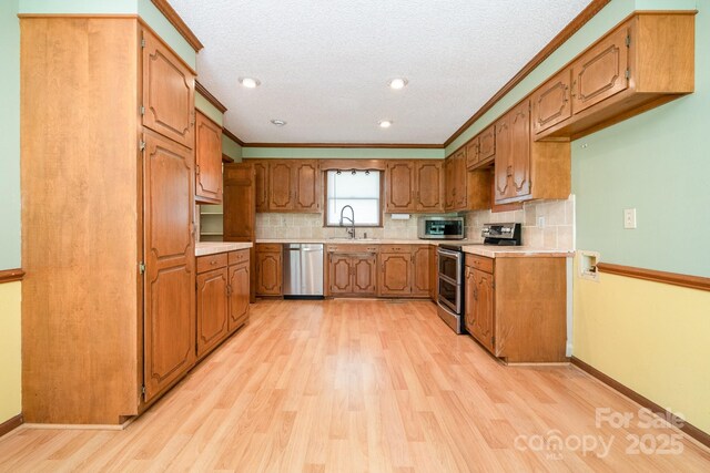 kitchen featuring brown cabinets, appliances with stainless steel finishes, light countertops, light wood-style flooring, and backsplash