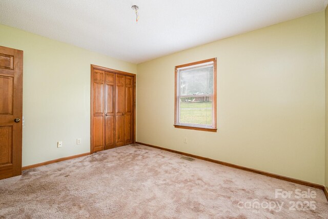 unfurnished bedroom with baseboards, a closet, light colored carpet, and visible vents