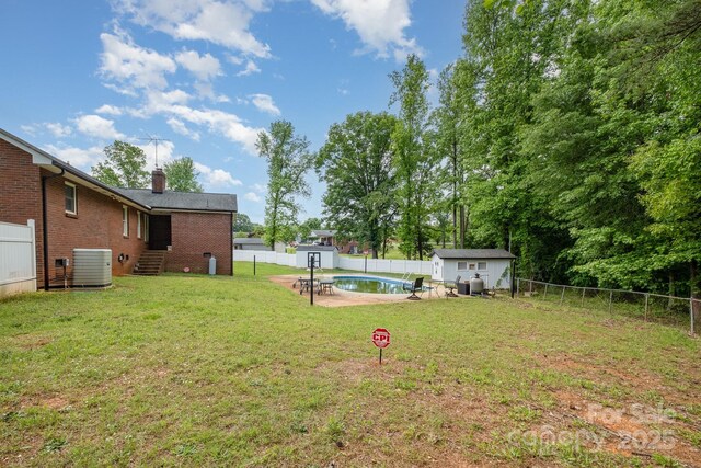 view of yard featuring a shed, a fenced backyard, a fenced in pool, an outbuilding, and central air condition unit