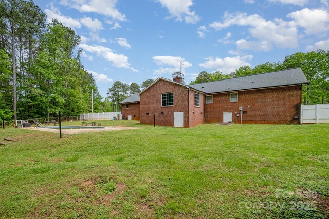 back of house featuring brick siding, a lawn, fence, and a chimney