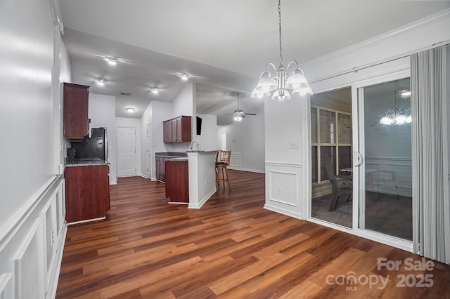 kitchen with a chandelier, a kitchen breakfast bar, a ceiling fan, dark wood finished floors, and a decorative wall