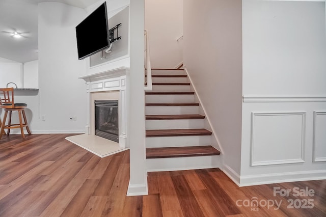 stairway with a glass covered fireplace and wood finished floors