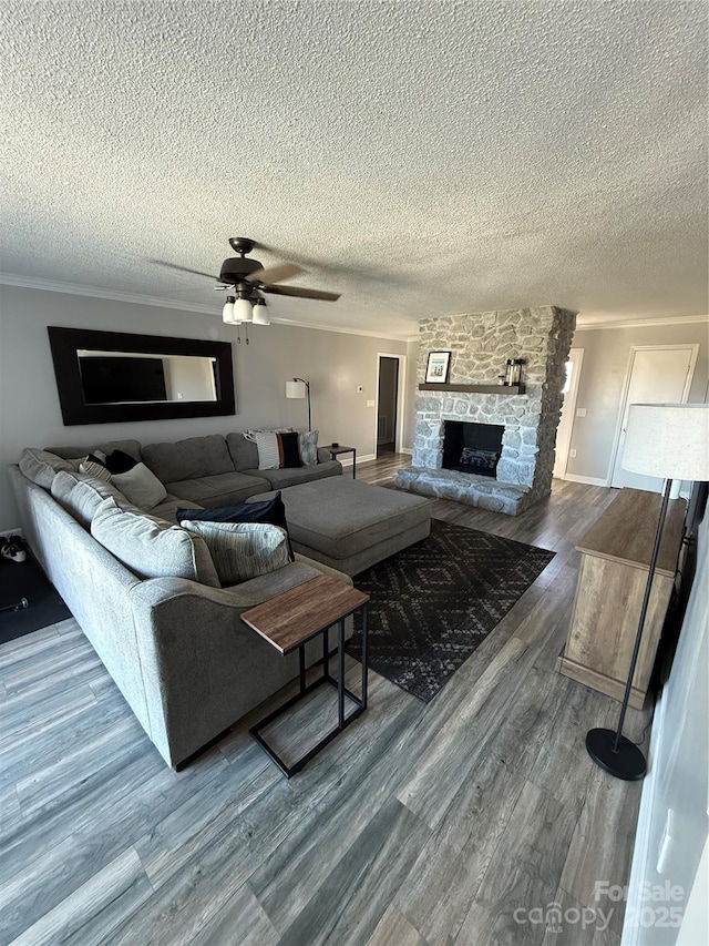 living area featuring a ceiling fan, a stone fireplace, wood finished floors, a textured ceiling, and ornamental molding