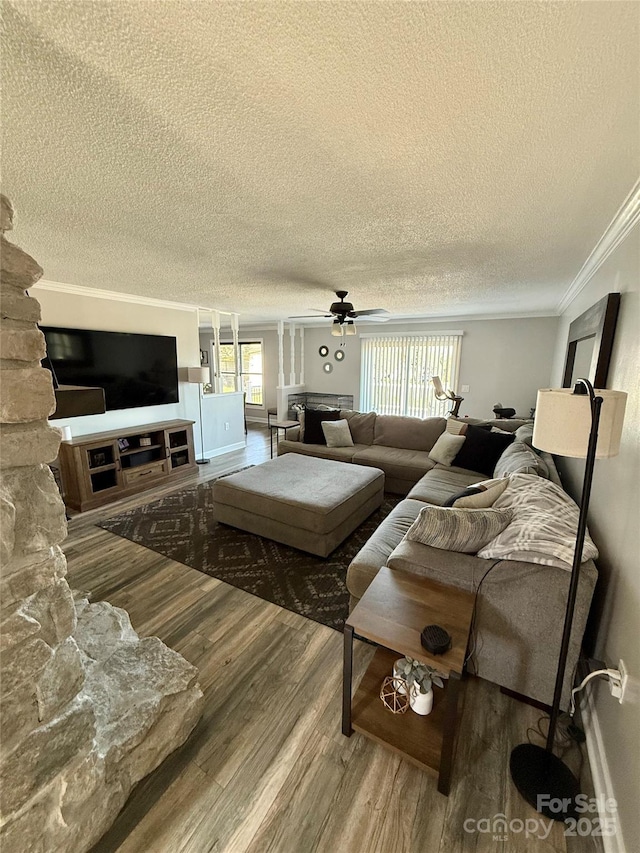 living room featuring a textured ceiling, wood finished floors, ceiling fan, a stone fireplace, and ornamental molding