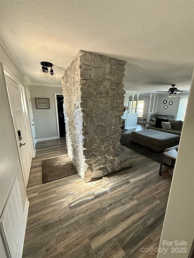 hallway with a textured ceiling, baseboards, visible vents, wood finished floors, and crown molding
